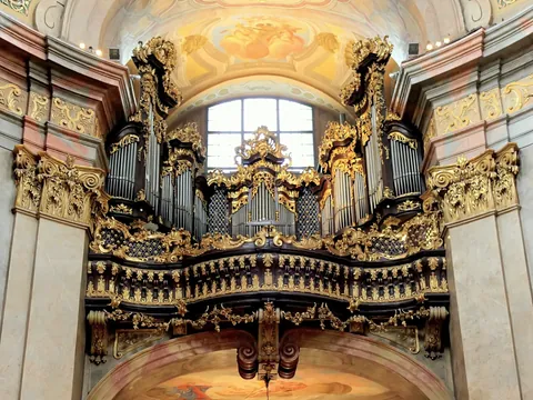Órgano barroco dorado de la Iglesia de San Pedro en Viena, con tubos metálicos y elaboradas decoraciones talladas bajo una bóveda pintada.