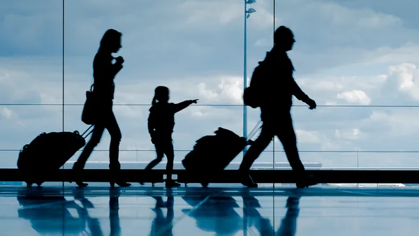 Familia en un aeropuerto, con maletas y equipaje, en una zona amplia con señalización y ventanales al fondo.