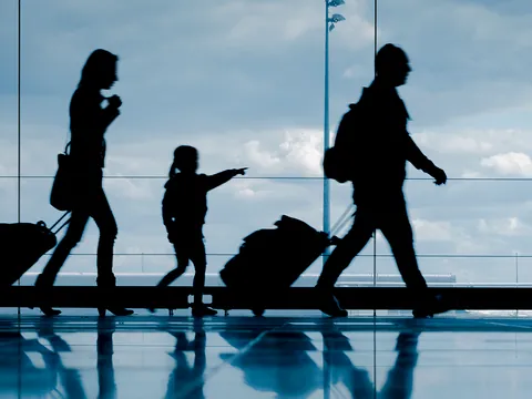 Familia en un aeropuerto, con maletas y equipaje, en una zona amplia con señalización y ventanales al fondo.