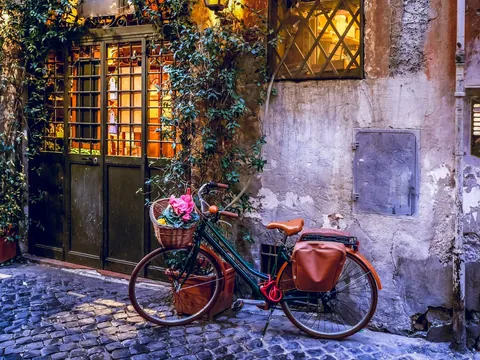 Bicicleta con flores apoyada en una fachada rústica iluminada en una calle de Roma
