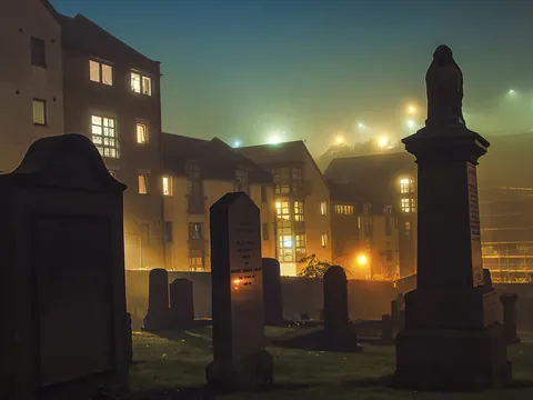 Old Calton Cemetery en Edimburgo iluminado por la noche con lápidas históricas y edificios de fondo