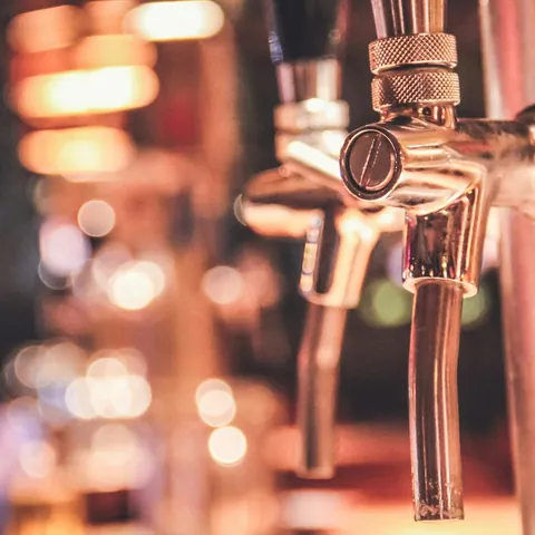 Grifos de cerveza metálicos en primer plano con bar de Berlín desenfocado.
