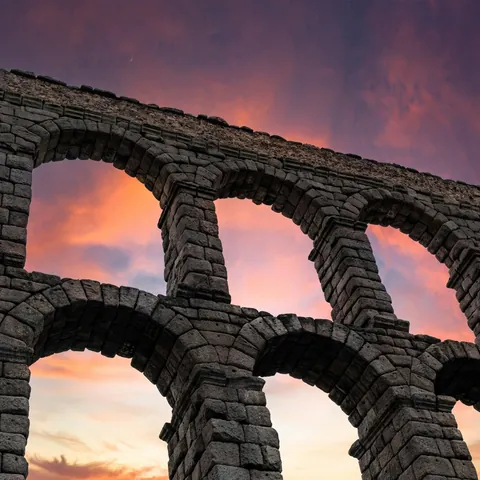 Arcos de piedra del Acueducto de Segovia bajo un cielo de atardecer rosado
