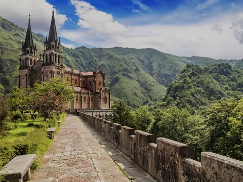 Santuario de Covadonga, Basílica de Santa María la Real, Asturias, rodeado de montañas verdes y cielo azul.