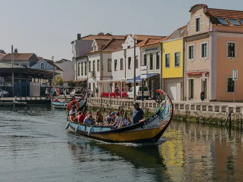 Moliceiro con turistas navegando por un canal de Aveiro junto a casas coloridas.