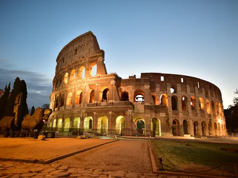 Coliseo de Roma iluminado al anochecer, mostrando su estructura ovalada y arcos icónicos en tonos cálidos.