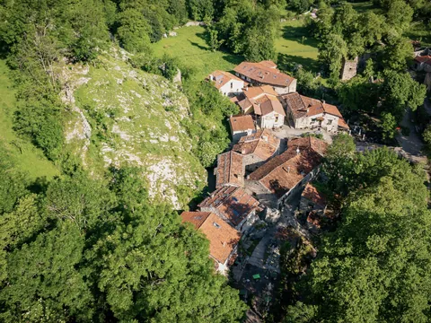 Vista aérea del pueblo de Bulnes, Asturias, en Picos de Europa, rodeado de vegetación verde y montañas.