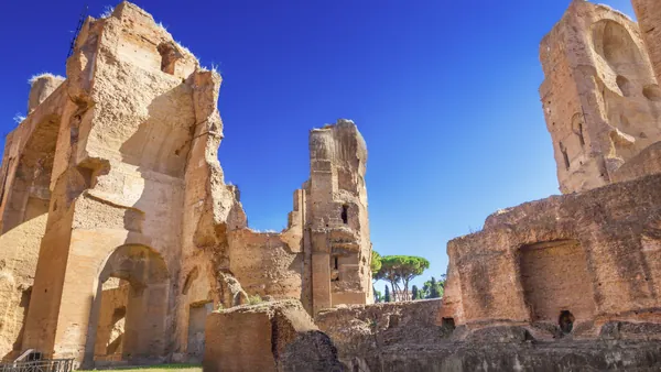 Ruinas de las Termas de Caracalla en Roma, con grandes muros de ladrillo, arcos monumentales y áreas verdes bajo cielo despejado.