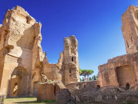 Ruinas de las Termas de Caracalla en Roma, con grandes muros de ladrillo, arcos monumentales y áreas verdes bajo cielo despejado.