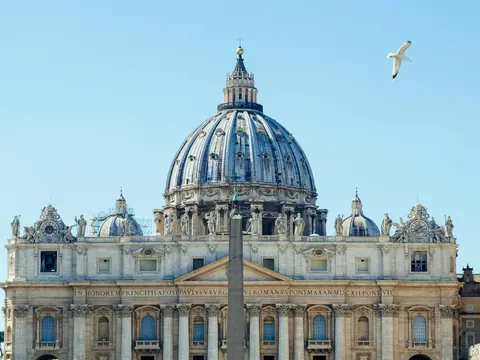 Cúpula y fachada de la Basílica de San Pedro en Ciudad del Vaticano, bajo cielo azul.