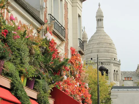 Vista parcial de la Basílica del Sacré-Cœur en Montmartre, París, con una fachada adornada con abundantes flores rojas y verdes en primer plano.