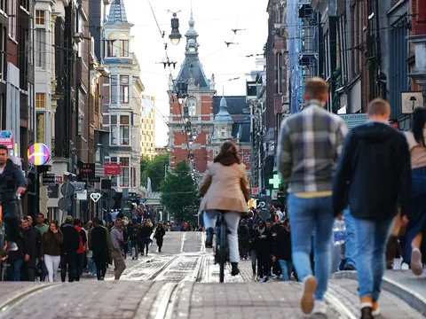 Calle concurrida de Ámsterdam con personas caminando y ciclistas rodeada de edificios históricos y tiendas.