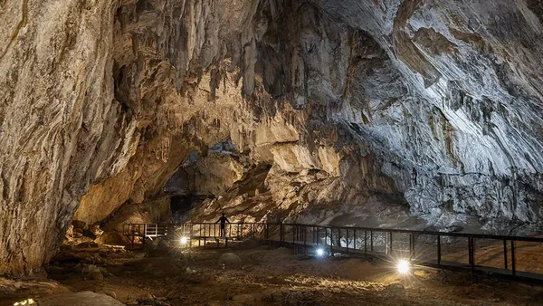 Interior de la cueva Cullalvera iluminado, con estalactitas y pasarela para visitantes en un amplio espacio