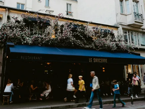 Fachada del restaurante Le Sancerre en París, con toldo azul oscuro y decoración floral abundante en el balcón superior, mientras varias personas caminan por la acera.