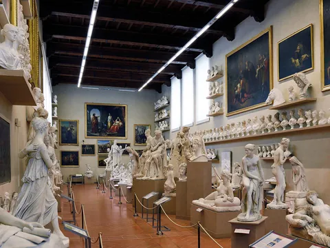 Sala del museo en Florencia con numerosas esculturas clásicas de mármol, bustos alineados en estanterías y grandes pinturas renacentistas colgadas en las paredes.