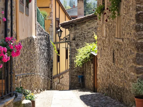 Calle empedrada con casas de piedra y flores en el casco histórico de Potes, Cantabria.