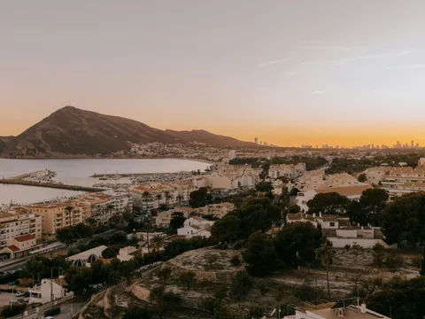 Vista aérea de Altea al atardecer, mostrando la costa, el puerto, las casas blancas y la montaña de fondo.