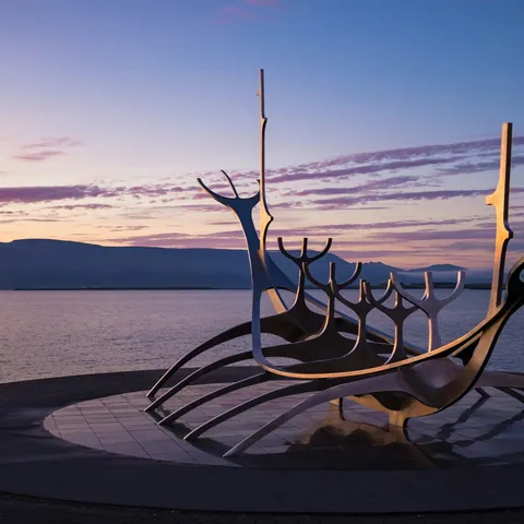 Escultura del Viajero del Sol en Reikiavik al atardecer, con vista al mar y montañas de Islandia iluminadas por el sol.