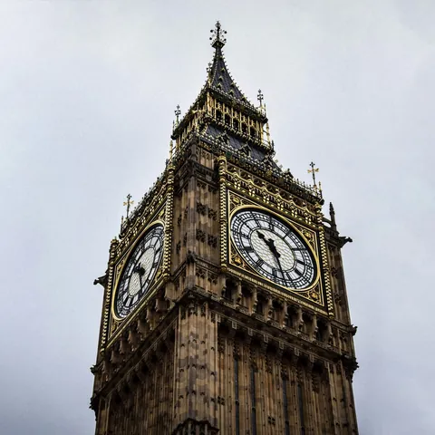 Primer plano de la Elizabeth Tower (Big Ben) en Londres, Inglaterra, con su reloj y detalles dorados bajo cielo nublado.