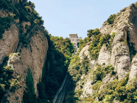 Funicular de Sant Joan subiendo por la grieta de roca de Montserrat, rodeado de vegetación y edificio en la cima.