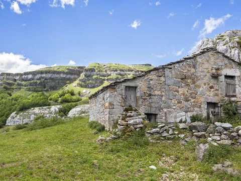 Cabaña de piedra tradicional en un valle verde, rodeada de montañas y naturaleza en Cantabria.