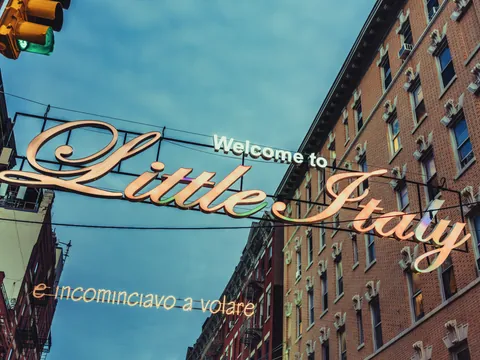 Cartel de bienvenida a Little Italy en Nueva York entre edificios de ladrillo con un cielo azul oscuro.