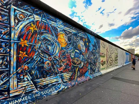 Colorido mural en el Muro de Berlín con motivos abstractos y personas observando la obra