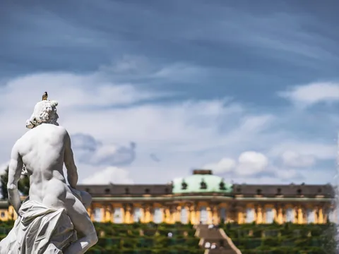 Estatua clásica con un pájaro en el Jardín de Sanssouci, Potsdam. Al fondo se ve la fuente y el Palacio de Sanssouci.