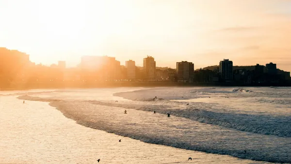 Atardecer en la playa de Gijón con olas y edificios junto al mar