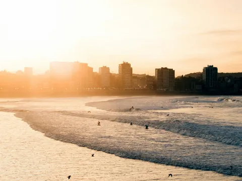 Atardecer en la playa de Gijón con olas y edificios junto al mar