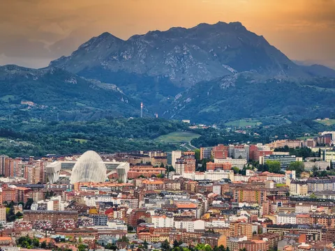 Vista panorámica de Oviedo con el Palacio de Exposiciones y Congresos y las montañas asturianas al fondo al atardecer.