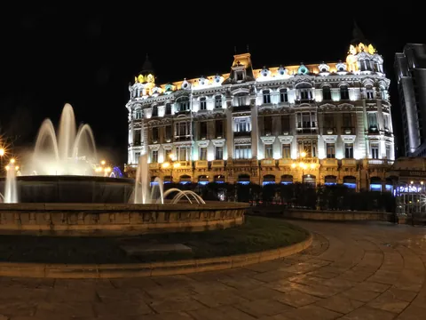 Fuente y edificio histórico de la Plaza de la Escandalera en Oviedo iluminados de noche, uno de los puntos más icónicos de la ciudad.