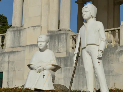 Estatua de los pastores Francisco y Jacinta Marto en Fátima, Portugal, sobre pedestal con columnas detrás.