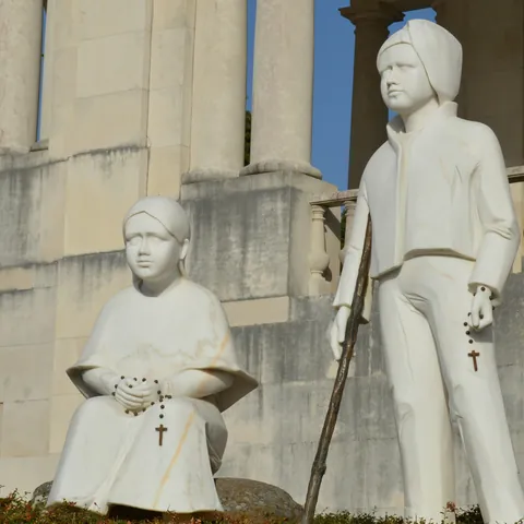 Estatua de los pastores Francisco y Jacinta Marto en Fátima, Portugal, sobre pedestal con columnas detrás.