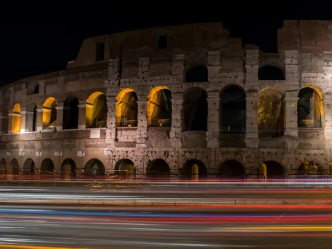 Coliseo de Roma iluminado de noche con estelas de luz de tráfico en la avenida