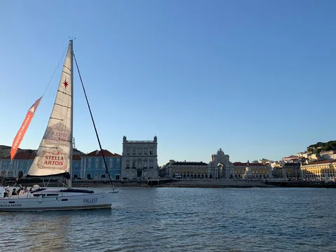 Velero navegando frente a la Plaza del Comercio en Lisboa al atardecer.