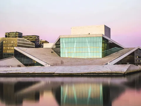 Ópera de Oslo, Noruega, al atardecer, con su arquitectura moderna reflejada en las tranquilas aguas del fiordo.