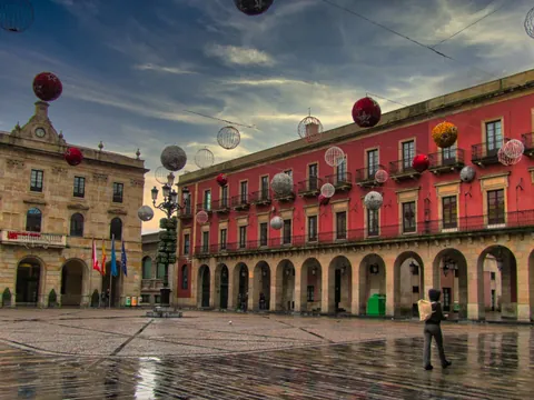 Plaza Mayor de Gijón con decoración navideña y edificios históricos, reflejados en el suelo mojado tras la lluvia