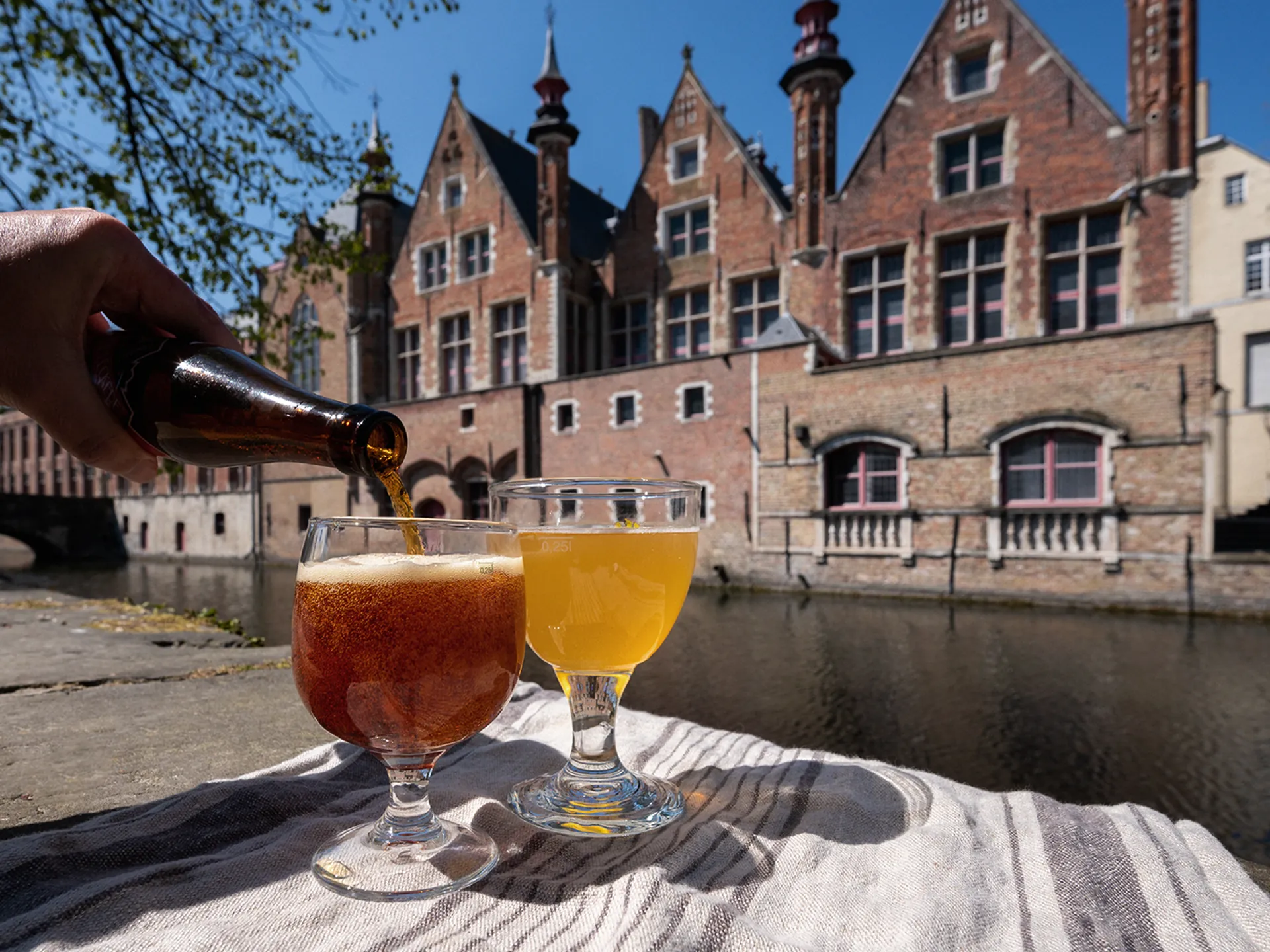 Persona sirviendo cerveza artesanal frente a canales y edificios de Brujas
