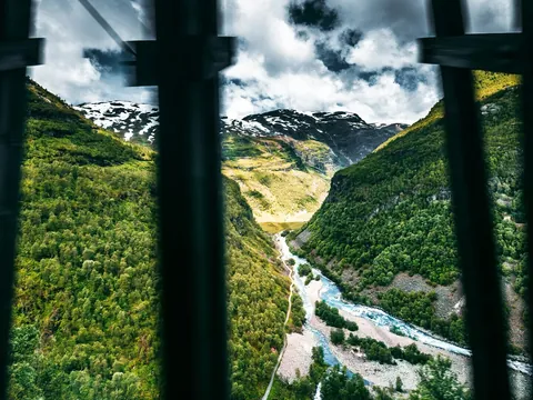 Vista impresionante del valle y río Kjosfossen desde Myrdal, Noruega, con frondosos bosques y montañas nevadas.
