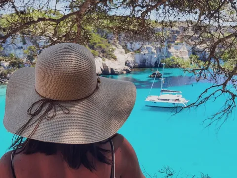 Mujer contemplando catamarán en Cala en Turqueta, Menorca