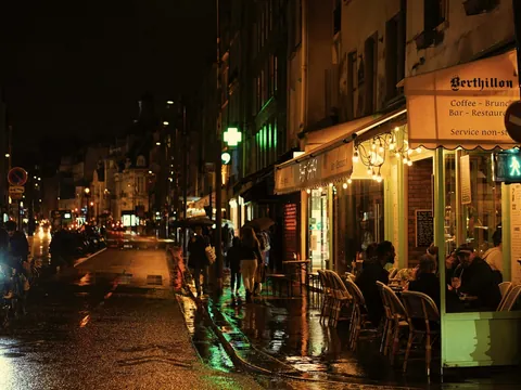 Gente cenando en la terraza iluminada del café Berthillon en una noche de París.