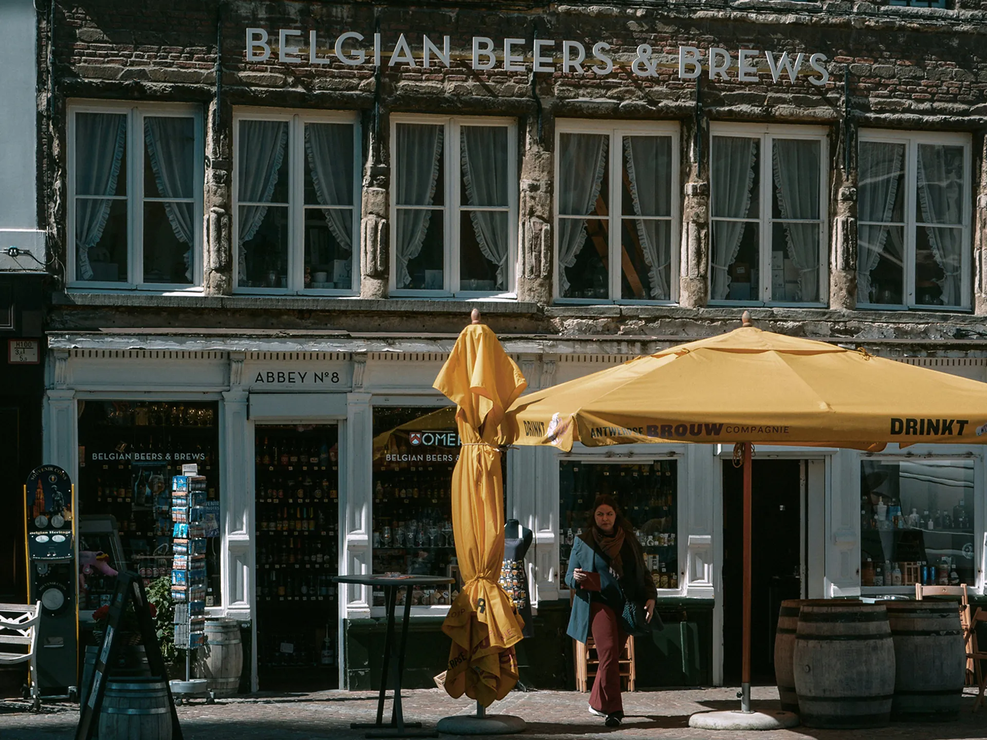 Cervecería belga con sombrillas amarillas en plaza histórica de Brujas. 