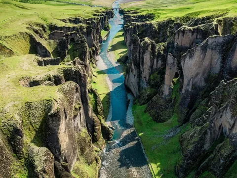 Vista aérea del cañón Fjaðrárgljúfur cerca de Kirkjubæjarklaustur, Islandia, con río azul entre acantilados verdes.