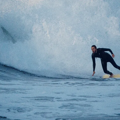 Surfista en traje de neopreno montando una tabla amarilla sobre una gran ola blanca y azul.