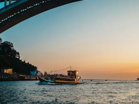 Barco turístico navegando al atardecer junto al puente de Arrábida en Oporto.