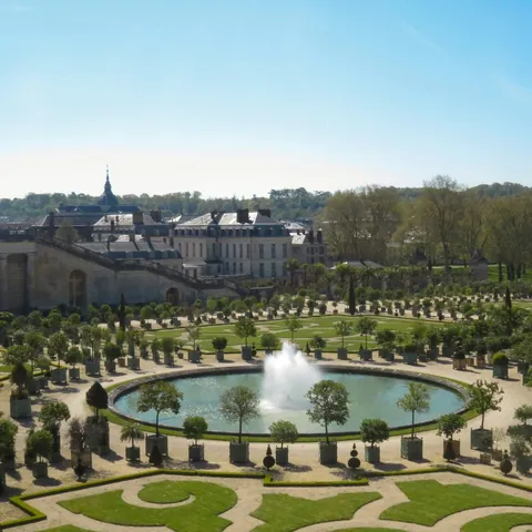 Jardines de Versalles, con fuentes, caminos simétricos y exuberante vegetación bajo un cielo despejado.