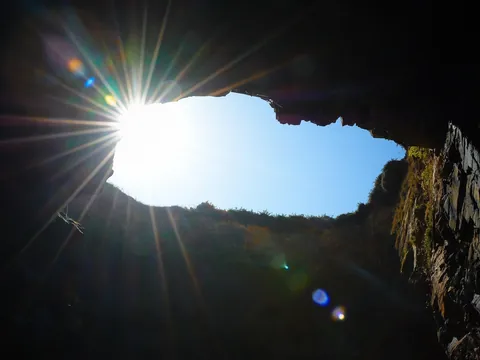 Interior de cueva en la Playa de las Catedrales, Ribadeo, Galicia, con el sol brillando intensamente.