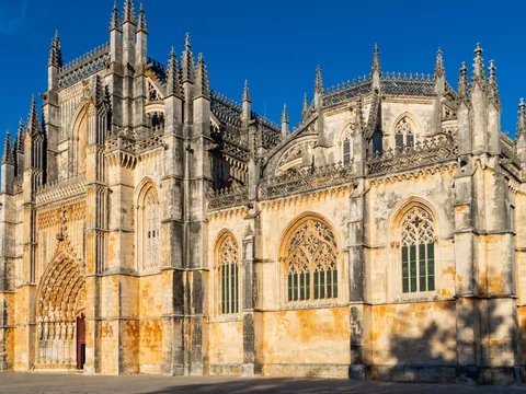 Fachada gótica del Monasterio de Batalha iluminada por el sol bajo un cielo azul.