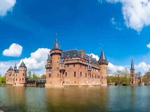 Vista panorámica del Castillo de Haar en los Países Bajos, rodeado por un foso de agua, con torres y muros de ladrillo rojo.
